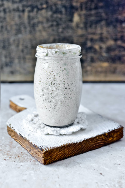 A dough starter in a glass jar sitting on a wooden board