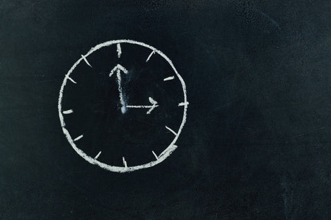 A clock drawn with chalk on a black chalkboard