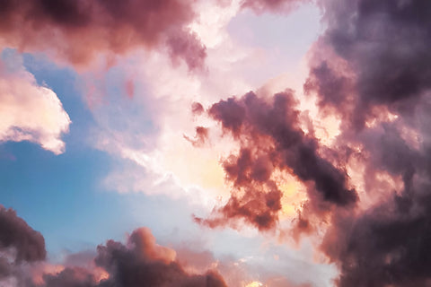 A blue sky with sun shining through pink clouds