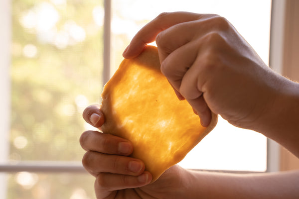 Hands stretching a small piece of dough to illustrate the windowpane test